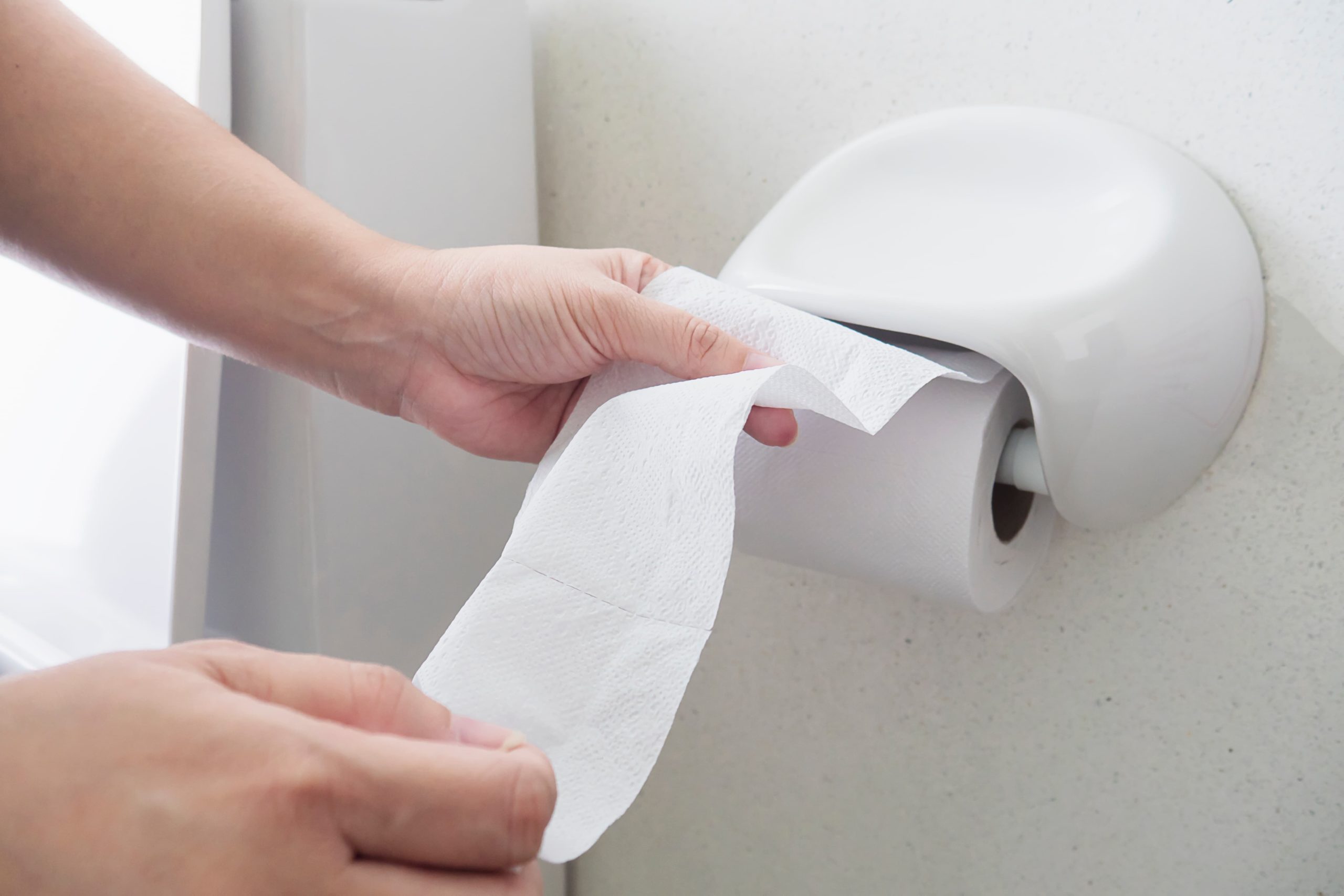Vaso entupido: mãos femininas retirando papel do rolo em uma cabine de banheiro